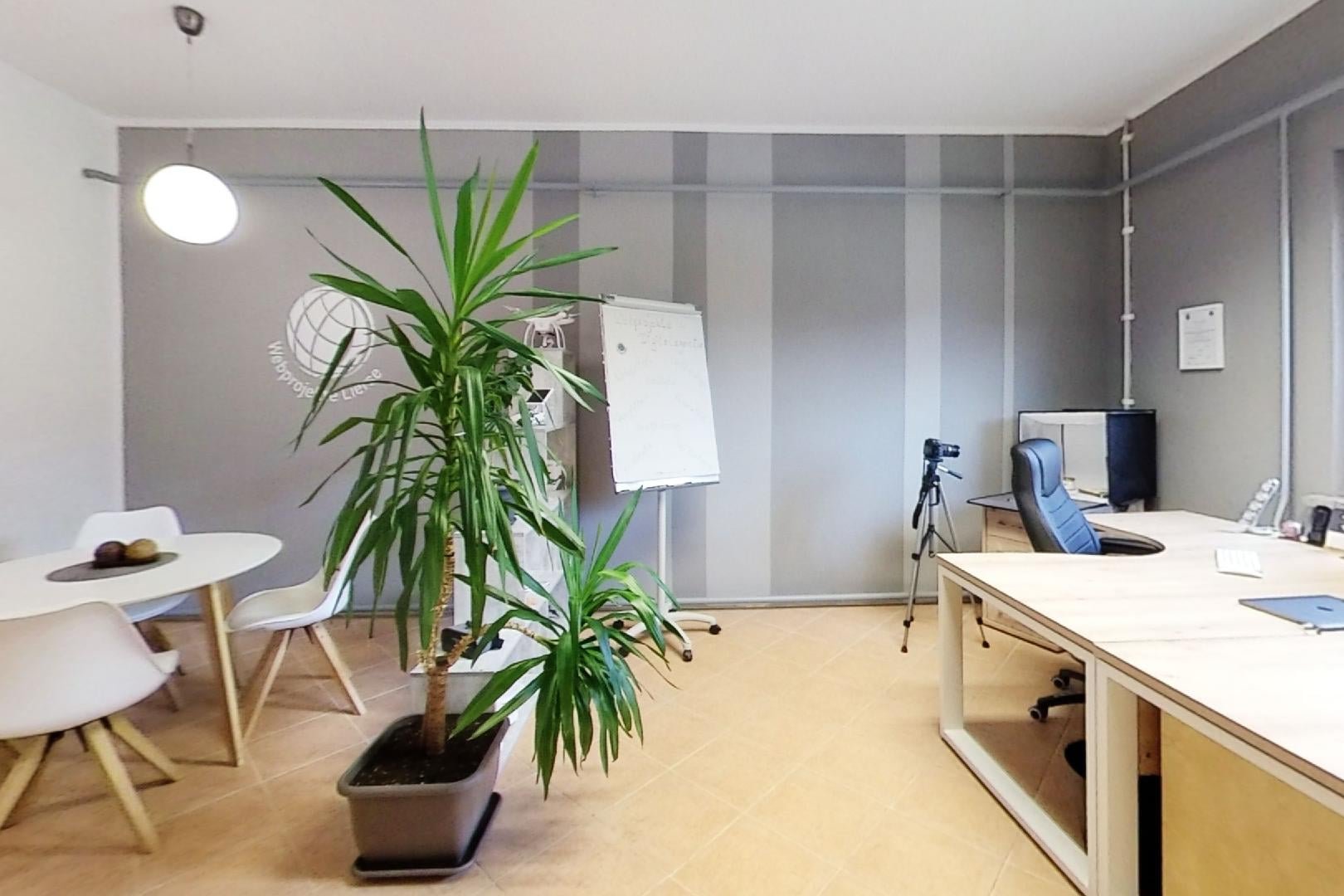 Helles Büro mit Schreibtisch, Computer, Stuhl, Flipchart und großen Zimmerpflanzen