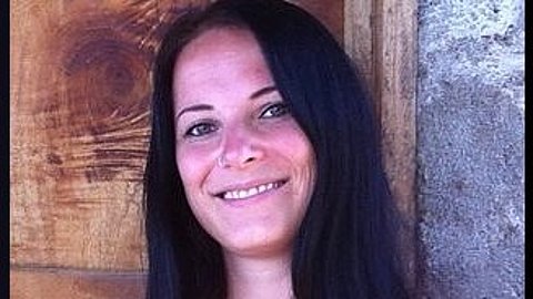 Carolin Müller in der Gründergalerie Frau mit langen schwarzen Haaren steht vor einer Holzwand links und einer grauen Wand rechts.