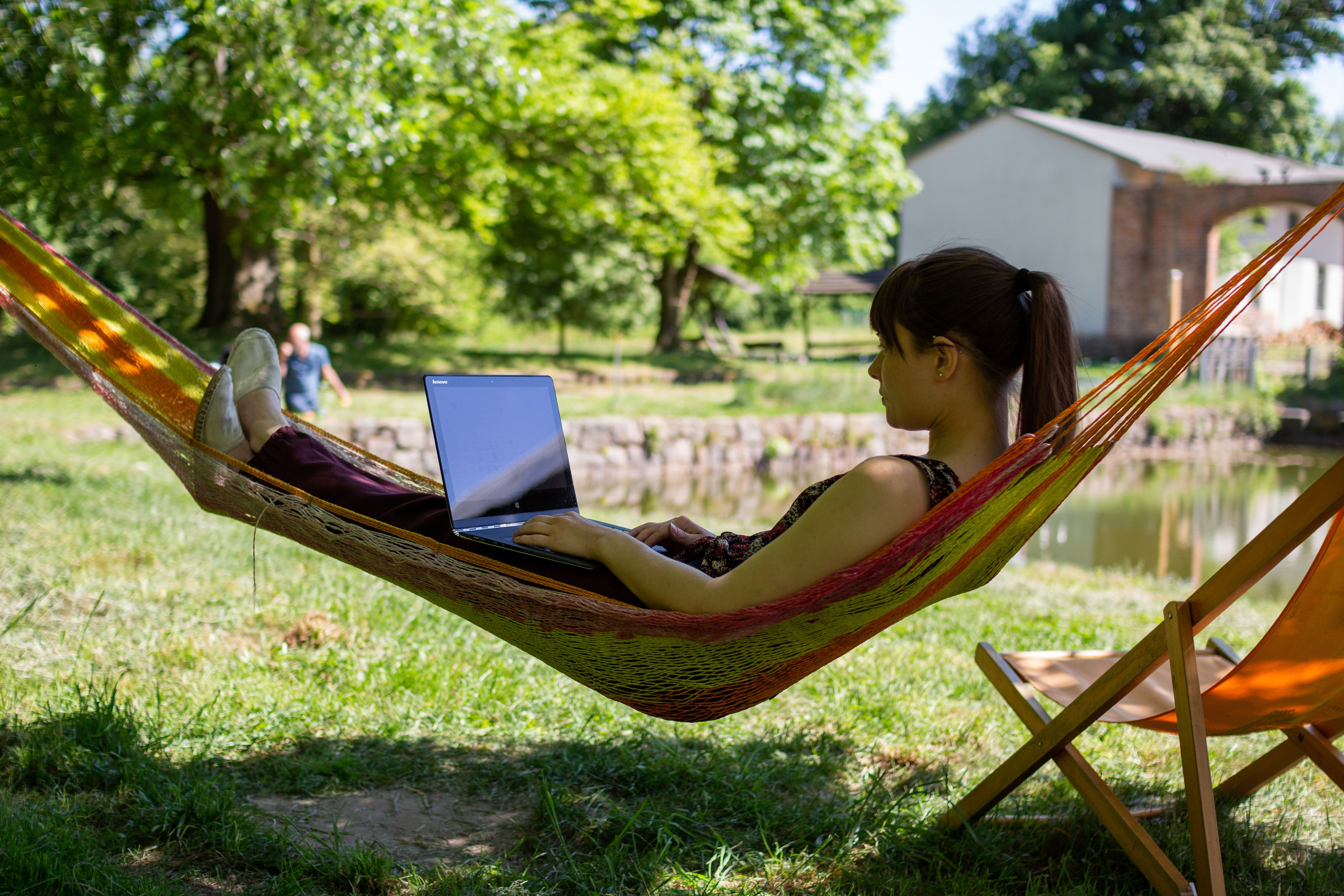 Person liegt in einer Hängematte im Garten und arbeitet an einem Laptop